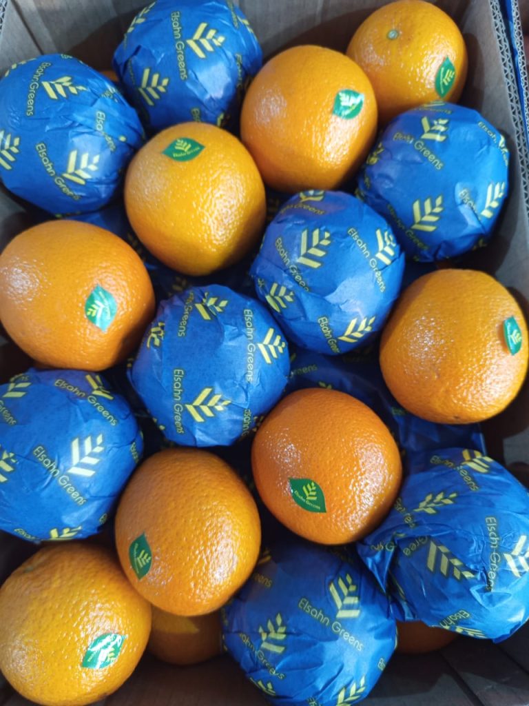 Close view of labelled oranges beside fruit in blue Elsahn Greens wraps